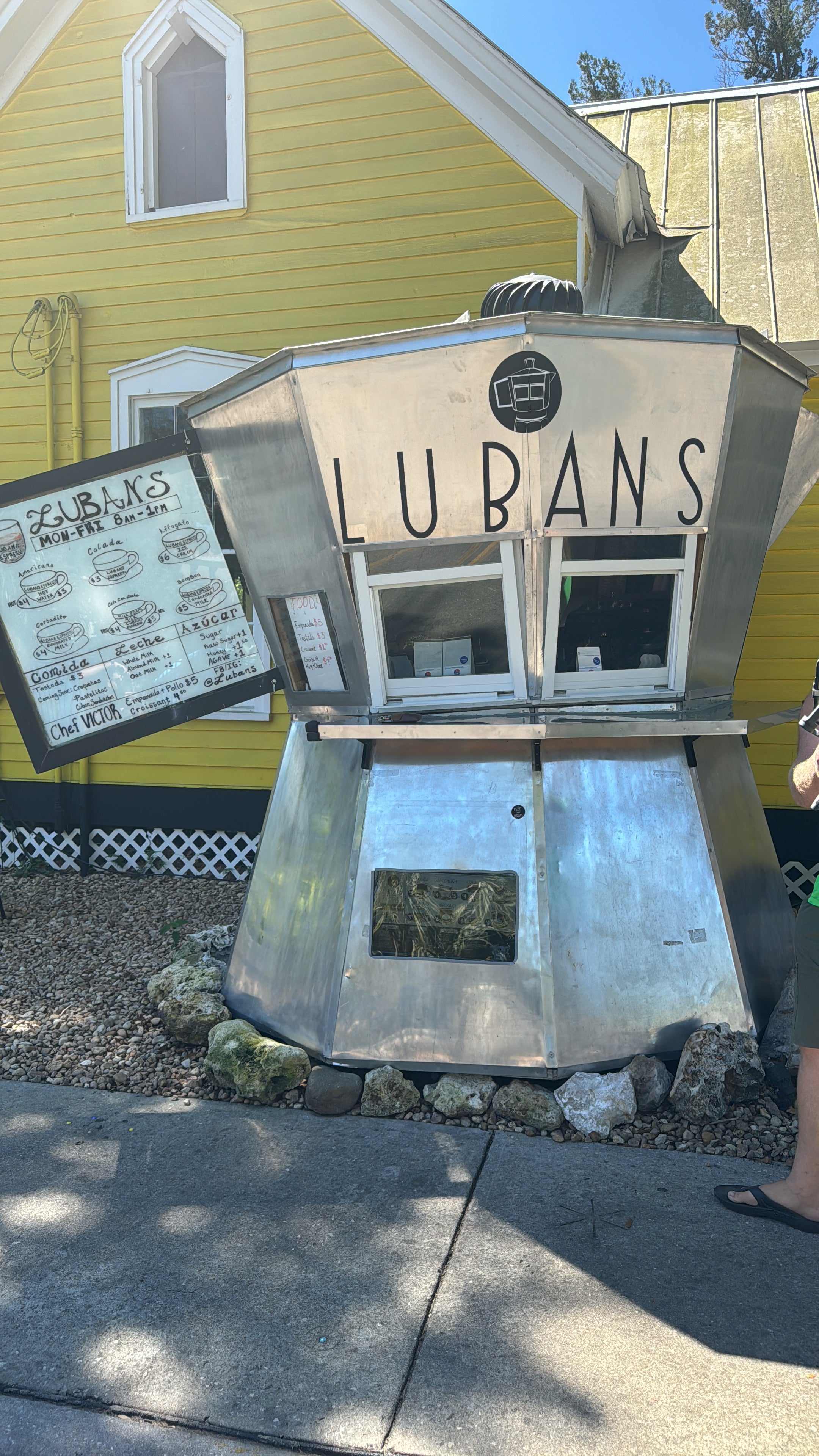 Lubans Coffee Co. Giant Cafetera outdoor espresso bar shaped like a cuban cafetera, serving Cuban-style coffee with a handwritten menu board outside a yellow building